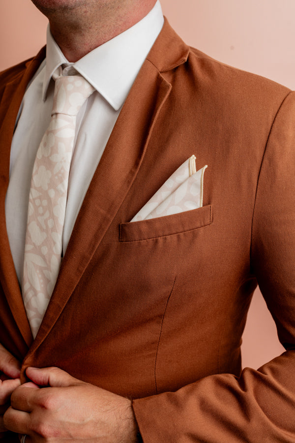 Stylish sand-colored pocket square with a unique cut-out pattern of white floral designs, perfect for adding a sophisticated touch to any formal outfit