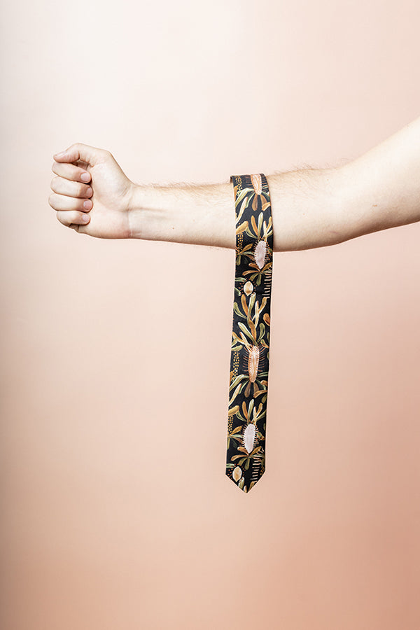 Stylish tie crafted from cotton, adorned with leafy designs in tones of burnt orange, sage green, and terracotta on a black background